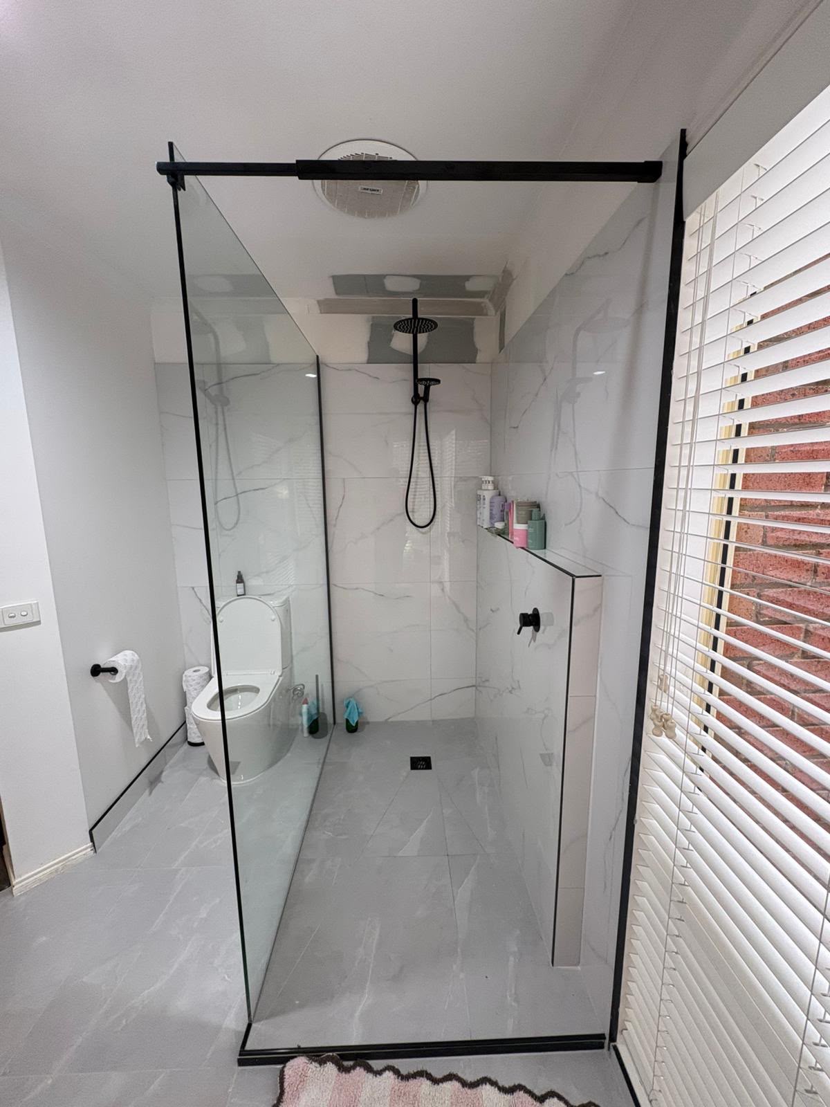 Walk-in shower with white marble-look tiling, black framed glass screen and black tapware