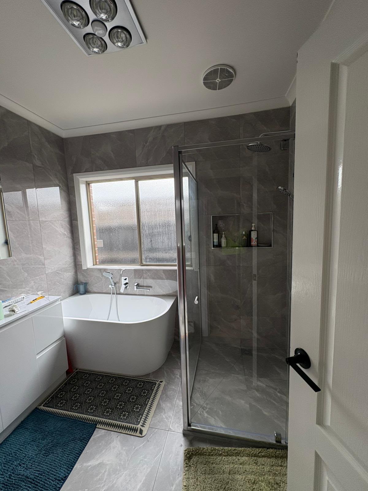 Grey stone-look tiled bathroom with freestanding bath and framed shower enclosure