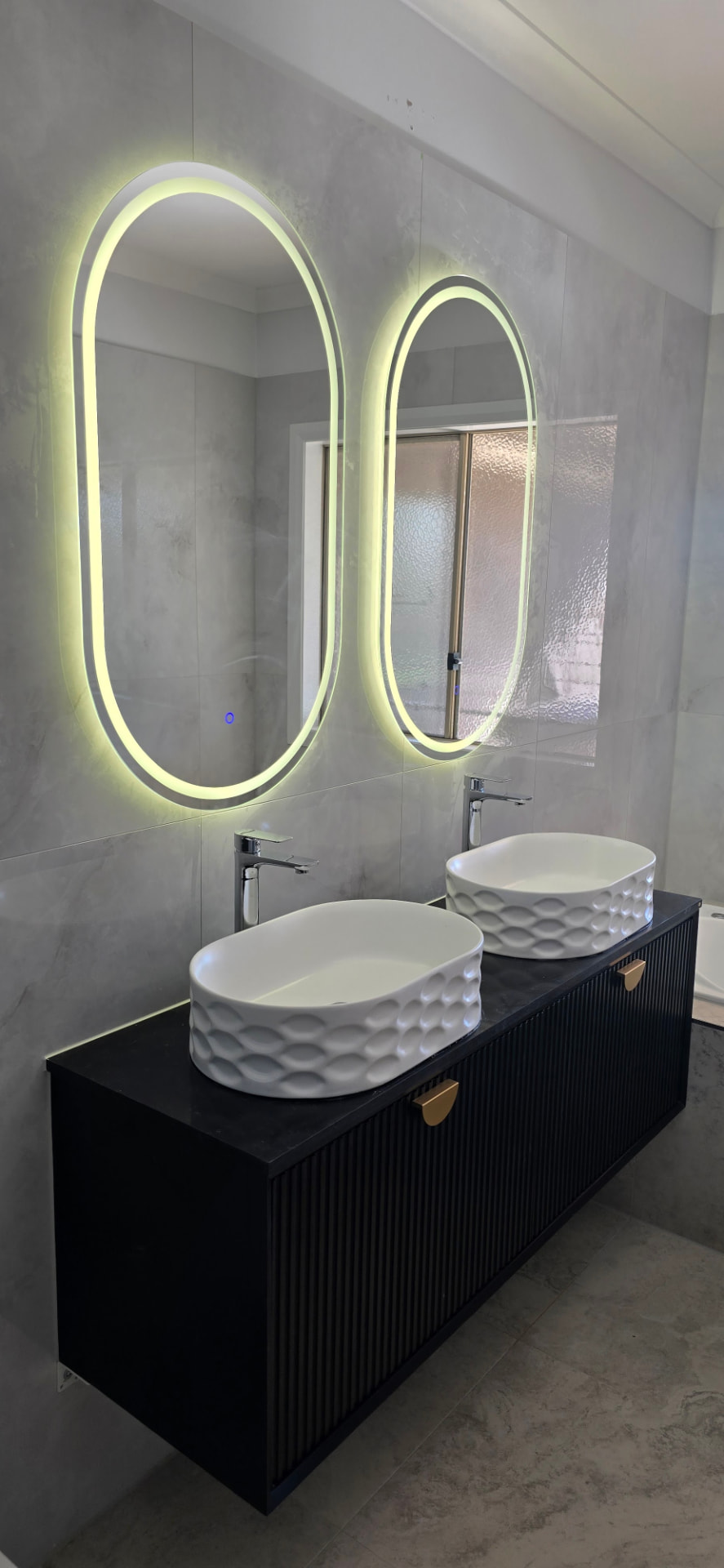 Renovated bathroom with black fluted vanity and backlit oval mirrors