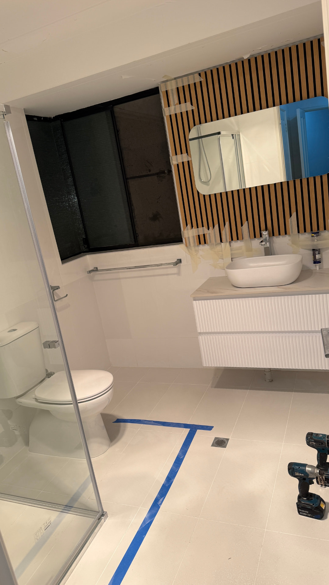 White fluted vanity with vessel basin and timber slat feature wall in a newly tiled bathroom