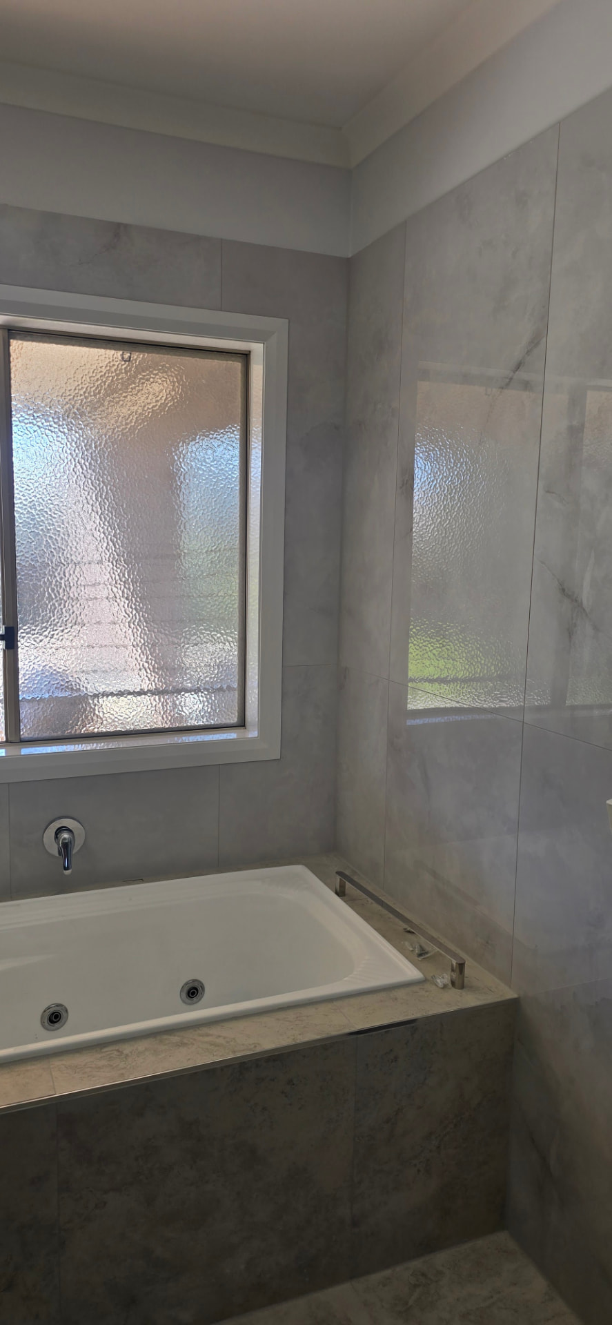 Bath surround tiled in large format marble-look tiles beside an obscure glass window